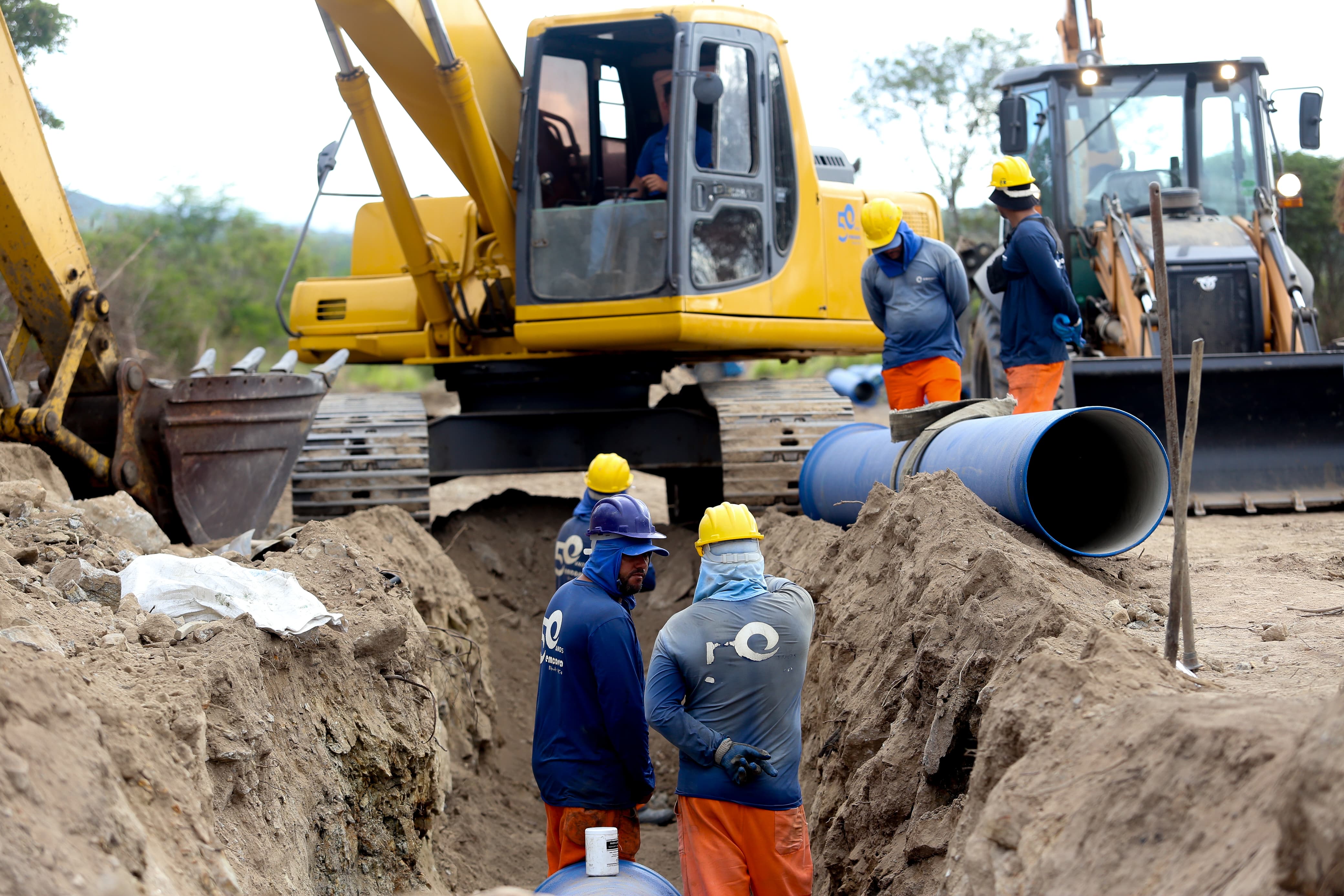 Foto da obra da Adutora do Agreste em Bezerros-PE. A foto apresenta máquinas e homens trabalhando em uma vala onde está sendo colocado colocado um cano para abastecimento de água.