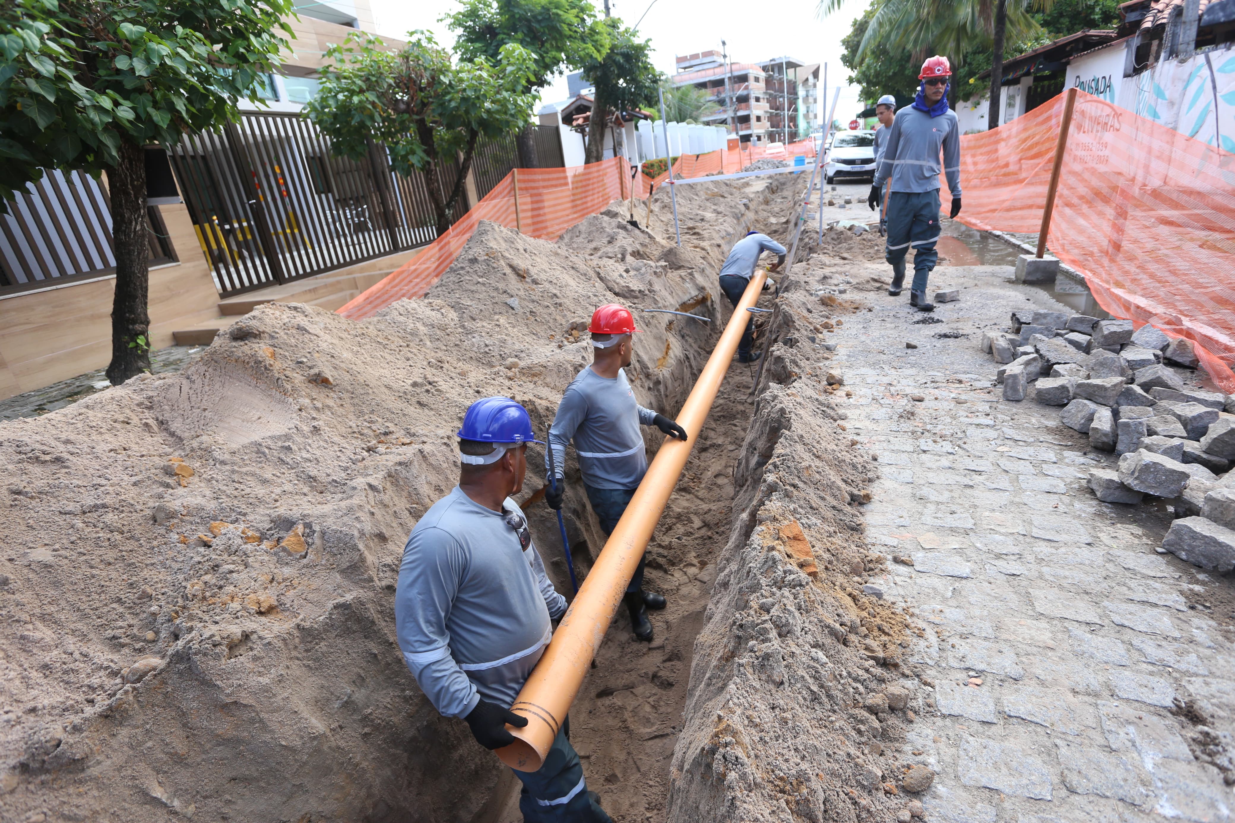 Foto da obra de esgotamento sanitário em Porto de Galinhas, Ipojuca-PE. A foto apresenta homens trabalhando em uma vala na calçada para colocação de tubulação.
