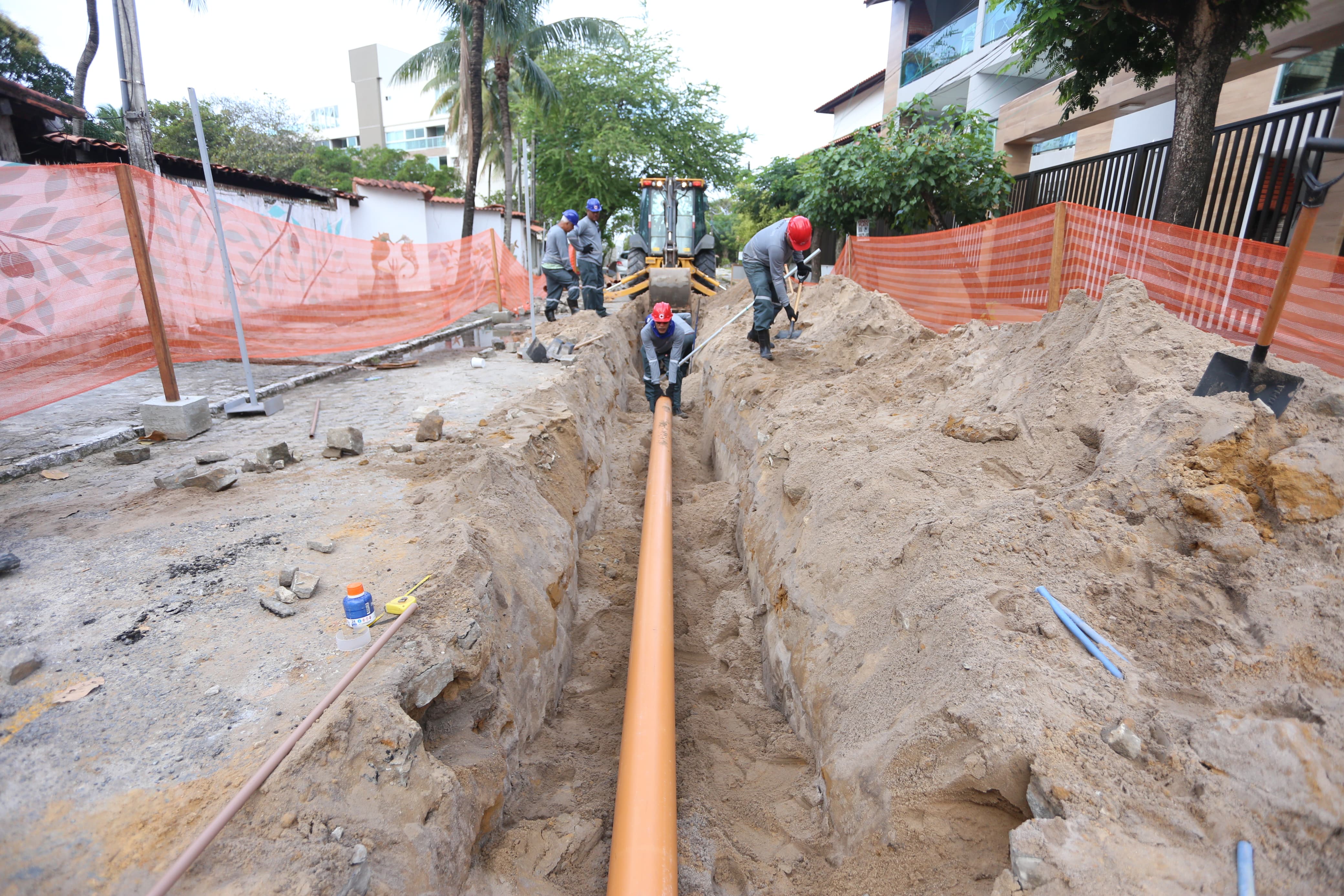 Foto da obra de esgotamento sanitário em Porto de Galinhas, Ipojuca-PE. A foto apresenta homens trabalhando em uma vala na calçada para colocação de tubulação.
