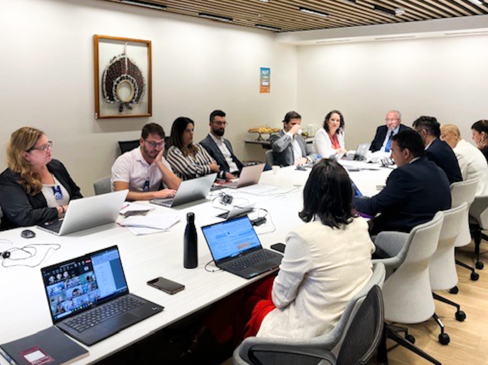 A foto apresenta uma sala de reunião, com pessoas sentadas ao redor de uma mesa.